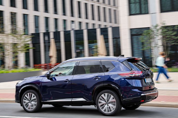 Seitliche Heckansicht eines Nissan X‑Trail, der durch städtische Umgebung fährt