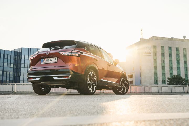 Blick von hinten unten auf einen parkenden Nissan Qashqai in Fuji Sunset Red, auf dem sich die tiefstehende Sonne bricht