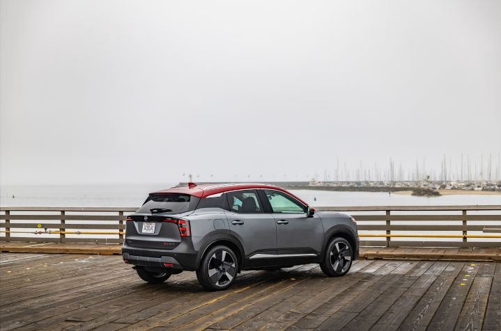 right rear 3/4 view of a silver 2025 Nissan Kicks parked on a boardwalk lot overlooking the ocean, a sailboat dock is behind.