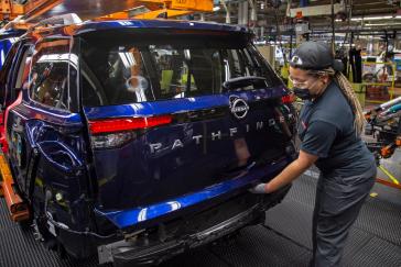 A Nissan worker fitting the rear hatch on a blue Pathfinder