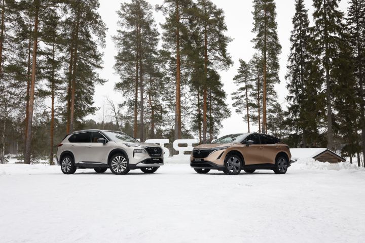 Silberner Nissan X‑Trail e‑Power e‑4ORCE und Elektroauto Nissan Ariya e‑4ORCE in Akatsuki Copper mit Dach und Außenspiegel in Pearl Black stehen nebeneinander auf schneebedecktem Untergrund