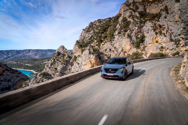 Vue dynamique du ¾ avant de l'Ariya NISMO sur une route de montagne avec vue sur le lac en arrière-plan.