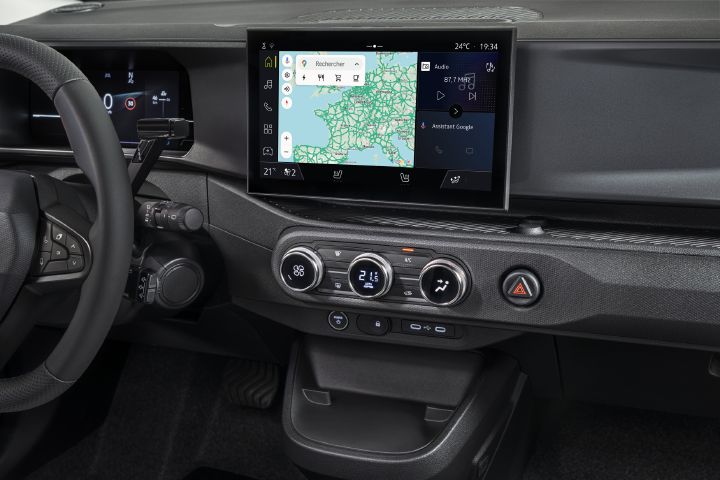 Photograph of a modern vehicle dashboard showing Google map, steering wheel, climate controls, hazard button, and storage compartment.
