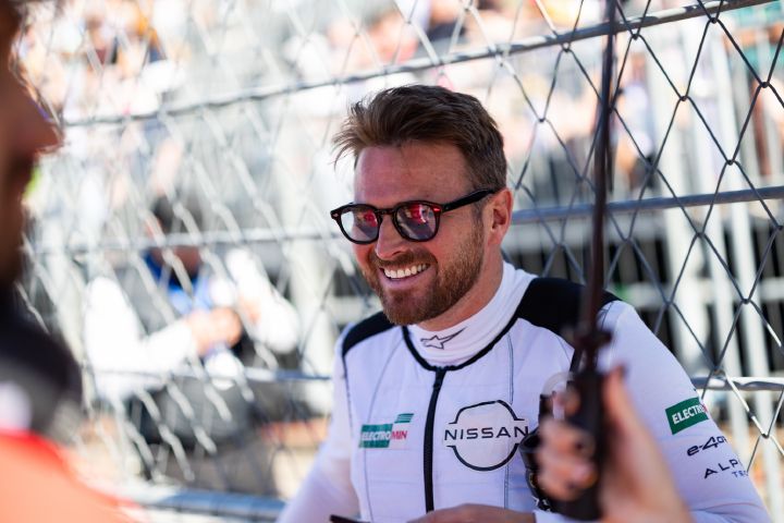 Oliver Rowland lächelt mit seiner Sonnenbrille und seiner weißen Kühlweste, während er in der Startaufstellung steht