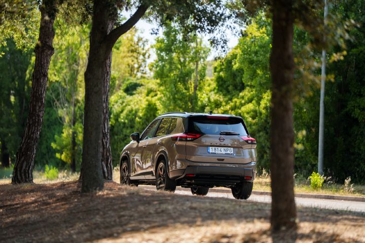 Dreiviertelansicht von hinten auf den Nissan X‑Trail durch Bäume hindurch