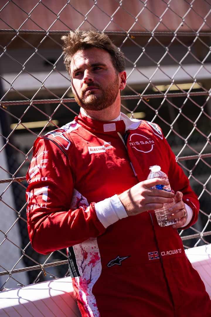 Porträtfoto von Oliver Rowland, der in seinem Nissan Formel E Rennanzug eine Wasserflasche in der Hand hält und an der Boxenmauer lehnt