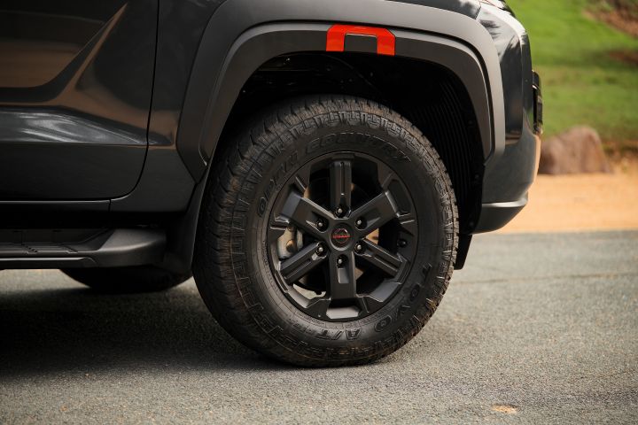 2026 Nissan Navara PRO-4X finished in Boulder Grey showing the matt black alloy wheel, all-terrain tyre, red-accented fender flare and side step.