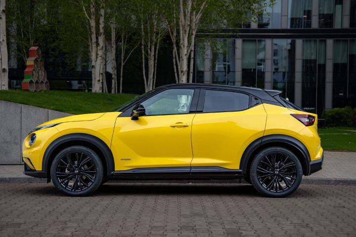 Żółty Nissan Juke stojący bokiem na tle budynku i drzew