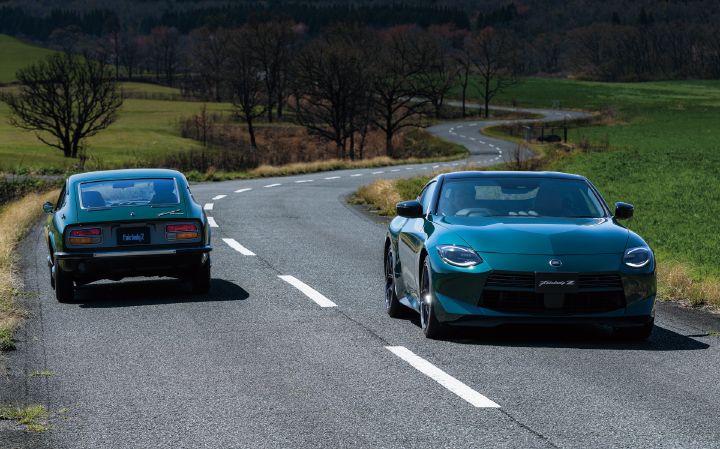 An Unryu Green Fairlady Z and a classic S30 Fairlady Z driving side by side on a gently winding country road. The modern Fairlady Z on the right is traveling toward the camera, showcasing its front fascia, large grille, and sleek coupe proportions. On the left, the first-generation S30 Fairlady Z is seen from the rear as it travels in the same direction, highlighting its distinctive tail design and classic styling. Open grasslands, scattered trees, and a winding road stretching into the distance create a scenic backdrop. The image emphasizes the contrast between the latest Fairlady Z and the iconic S30 generation, celebrating the heritage and evolution of the Fairlady Z lineage.
