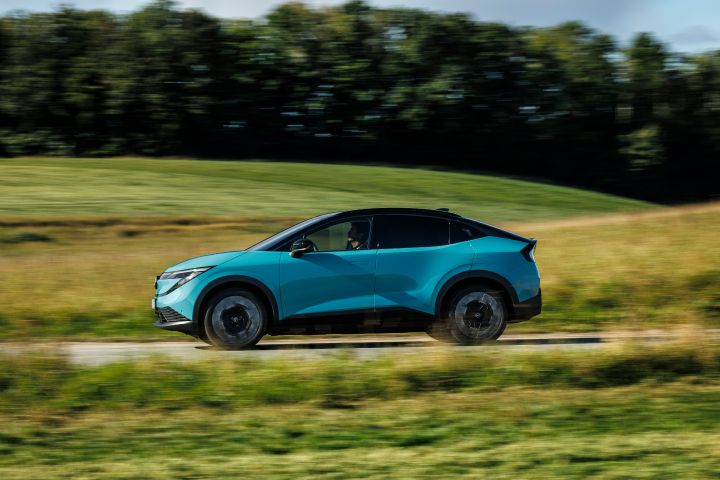Seitliche Fahraufnahme eines türkisen Nissan LEAF, der ländliche Hintergrund ist nur verschwommen zu sehen
