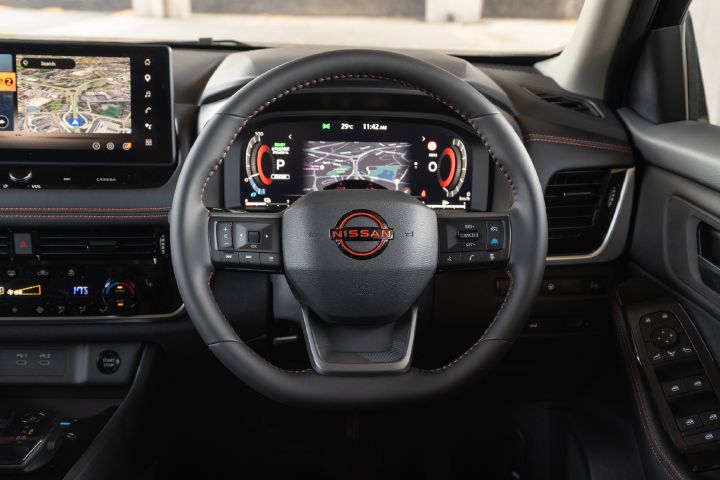 Close-up view of the Nissan X‑Trail driver's area, featuring the multifunction steering wheel, digital driver display and central touchscreen with navigation.