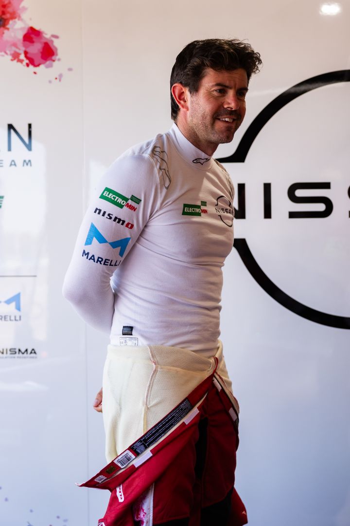 Porträtfoto von Norman Nato, der in der Nissan Teamgarage steht mit heruntergeklapptem Rennoverall und weißem Shirt.