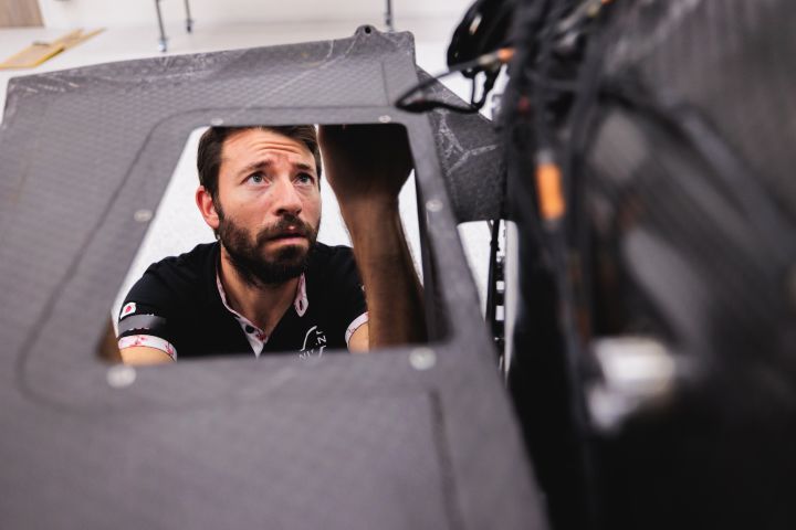 Blick durch ein Karbonteil eines Nissan Formel E Rennwagens auf das konzentrierte Gesicht eines Mechanikers
