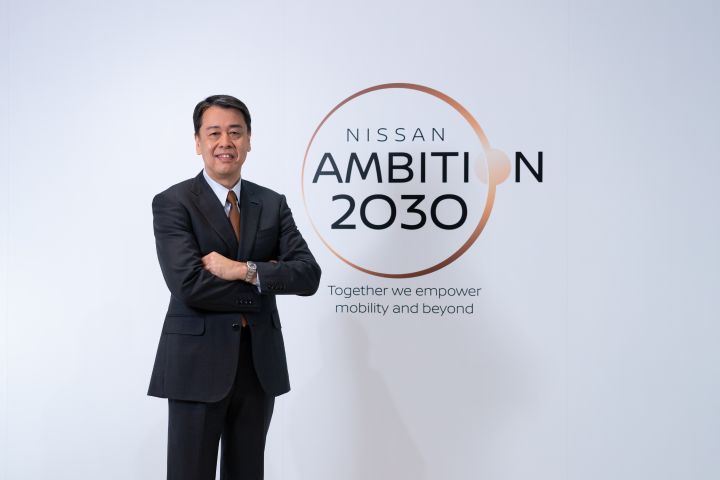 Nissan Ambition 2030ロゴの左側に立つ日産CEOうちだ まこと（腕組み）