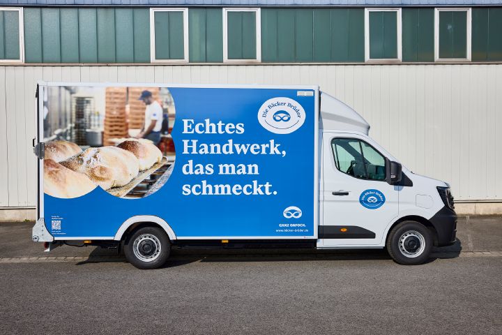 Statische Seitenansicht des Nissan Interstar-e mit blau-weißer Beklebung auf dem Bäckereikoffer und dem Schriftzug "Unser Brot fährt mit Sonne".