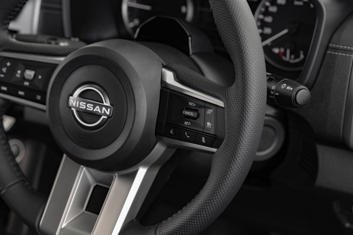Close-up of the steering wheel in a 2026 Nissan Navara ST-X, showing the Nissan badge, multi-function buttons, cruise-control controls, and part of the analogue instrument dials behind it.