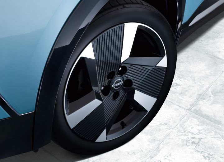 Close-up of the wheel of a bluish Nissan Kicks. The tire and distinctive wheel design are shown from the side.