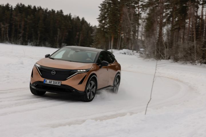 Elektroauto Nissan Ariya e‑4ORCE in Akatsuki Copper mit Dach und Außenspiegel in Pearl Black fährt auf Schnee, 3/4 Front