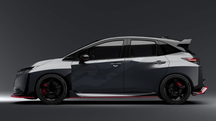 A silver and black two-tone sports car, the Aura Nismo RS Concept, photographed in a studio from a full side view. The vehicle is stationary, featuring a low stance and a large rear wing. The wheels are black with visible red brake calipers. The side displays a light gray 'RS,' and a red accent line runs along the lower body. The background is a simple gray gradient, highlighting the car's sleek and aggressive design