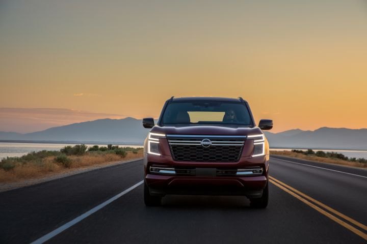 Front view of a 2025 Nissan Armada driving on a road during sunset with a mountain and body of water behind.
