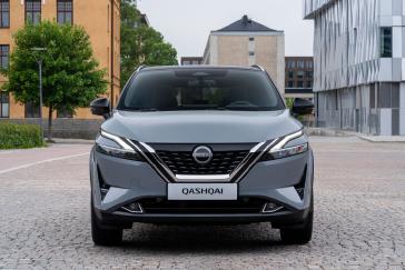 Nissan QASHQAI grise vue de face garée sur une route en briques avec des bâtiments en arrière-plan.