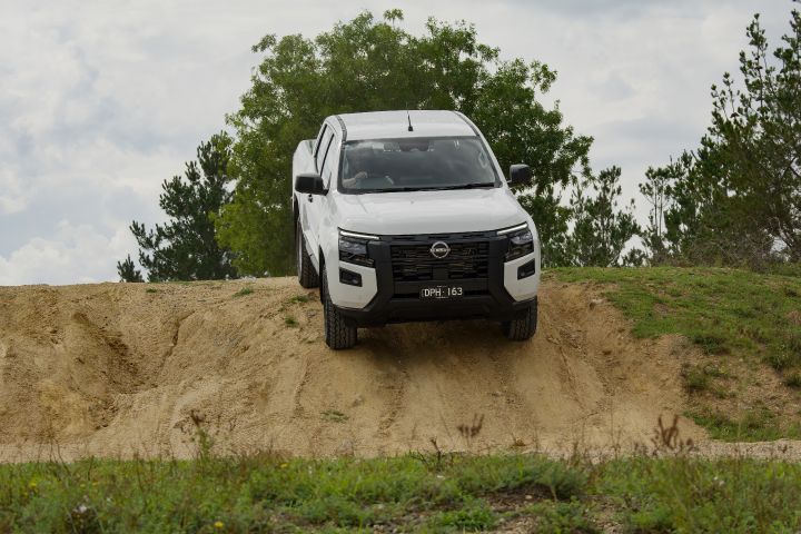 2026 Nissan Navara SL dual cab ute finished in Alpine White captured head-on while descending a sandy bank, showing the black grille and controlled off-road stance.