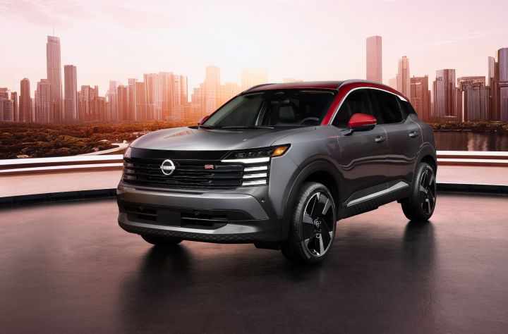 Front left 3/4 shot of a silver 2025 Nissan Kicks parked on concrete against a cityscape.