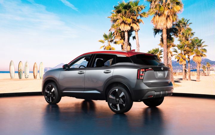 Rear left 3/4 view of the 2025 Nissan Kicks parked against a blue sky, palm trees and ocean water.