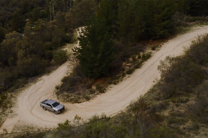 2026 Nissan Navara ST dual cab ute finished in Summit Silver seen from a high aerial angle turning through a sandy bush track.
