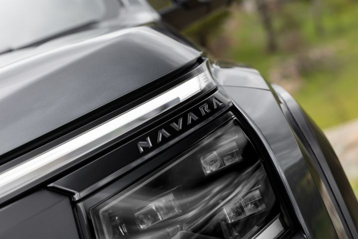2026 Nissan Navara PRO-4X finished in Boulder Grey showing the headlight cluster with NAVARA lettering, slim upper LED light and dark trim.