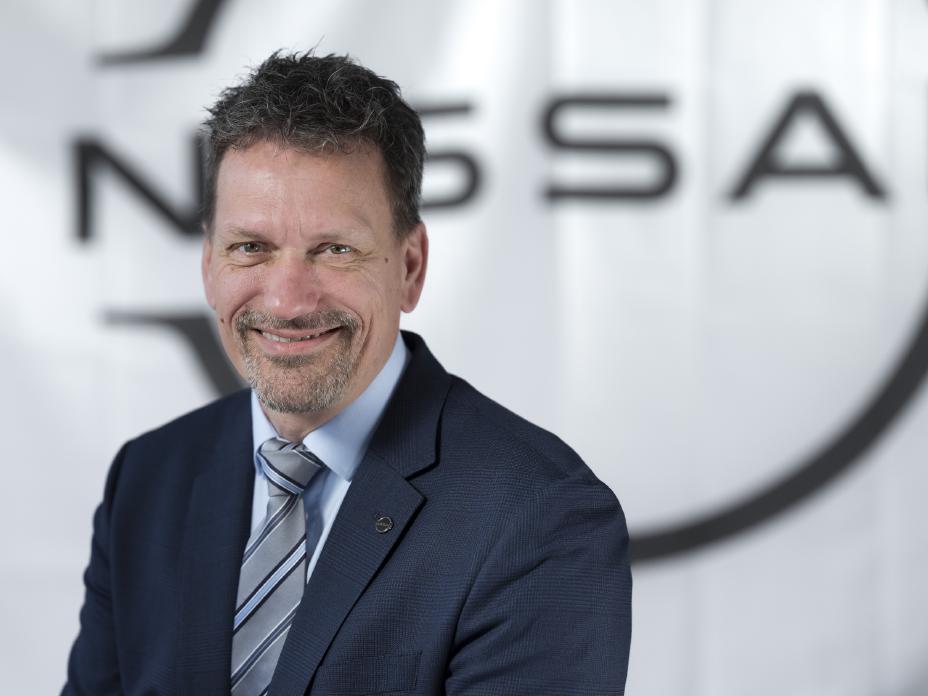 Porträtfoto des lächelnden Lars Ekering mit dunklem Anzug, hellblauem Hemd und Krawatte vor einer weißen Wand mit Nissan Logo