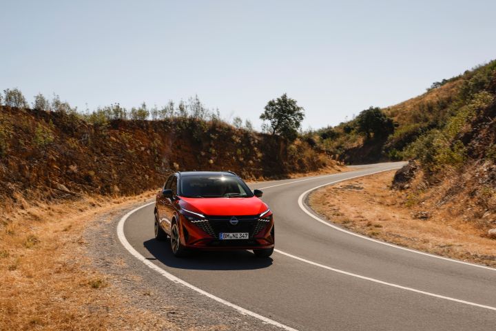 Front view of New refreshed Qashqai 2024 in fuji sunset color driving on a road in Faro, Portugal featuring the boomerang front led lights and grille