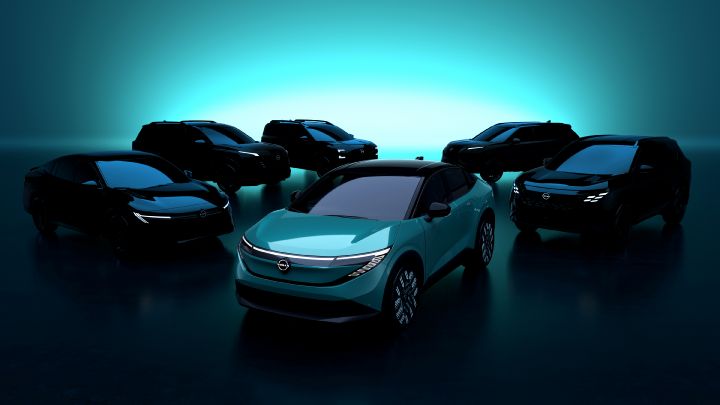 Five shaded Nissan cars all stand facing towards another Nissan car under light.