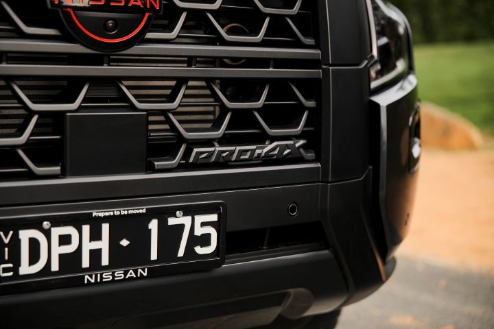 2026 Nissan Navara PRO-4X finished in Boulder Grey showing the lower front grille with PRO-4X badge, parking sensor, number plate and black bumper trim.