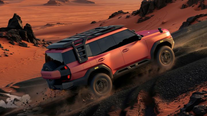 A red Terrano PHEV Concept seen from a rear three-quarter view, driving uphill to the right across a desert landscape at sunset. Sand dunes and rocky terrain surround the vehicle, with distant mountains in the background.