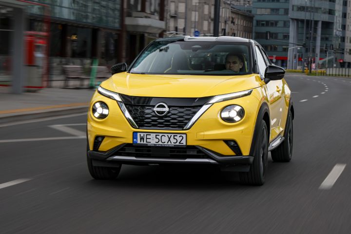 Jadący żółty Nissan Juke (widok z przodu) z budynkami w tle