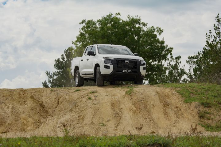 2026 Nissan Navara SL dual cab ute finished in Alpine White viewed head-on at the crest of a steep dirt embankment, emphasizing ground clearance and approach angle.