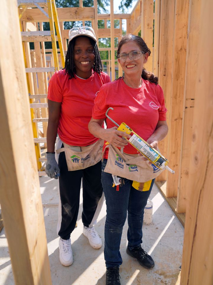 Two Nissan employees smile and pose together inside a house frame