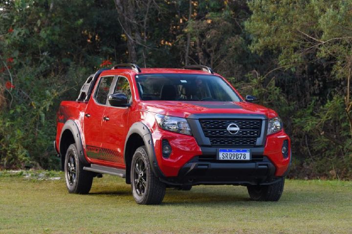 Picape Nissan Frontier Attack vermelha em um ambiente ao ar livre, destacando seu design e detalhes off-road.