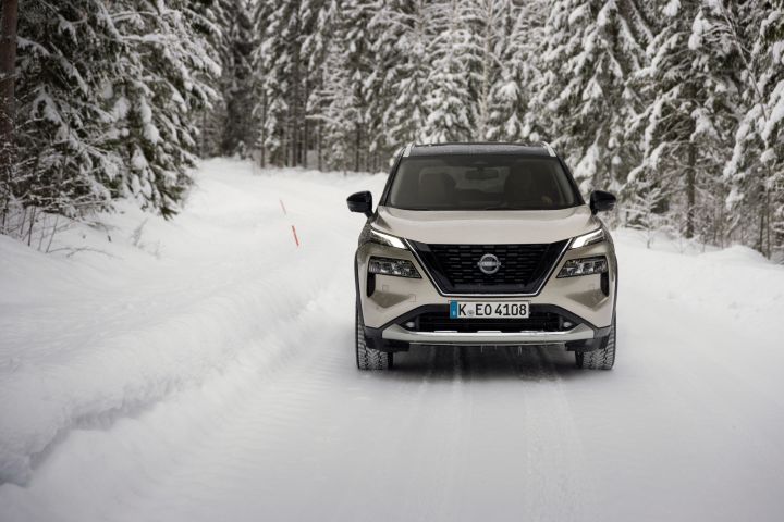 Silberner Nissan X‑Trail e‑Power e‑4ORcE fährt auf schneebedeckter Straße mit verschneiten Bäumen auf beiden Seiten, Front