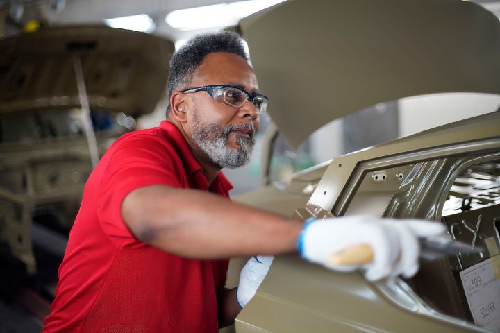 Image of a manufacturing team member with one arm reaching towards the door of a brown vehicle