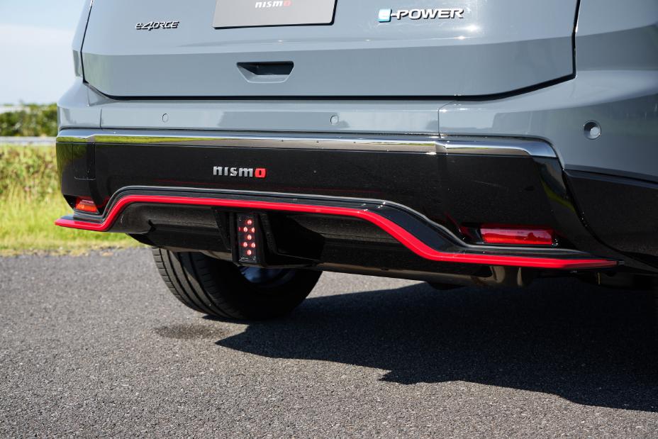 The lower rear bumper of a grey Nissan X-Trail NISMO is shown. The bumper features a black and red design with the word “SPORT” written in white letters on a black background. A tow hitch is visible below the bumper.
