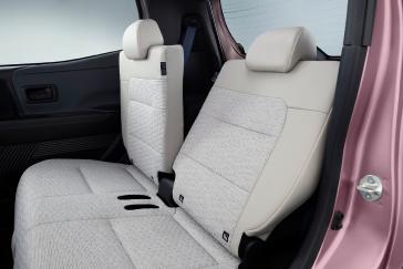 「日産サクラ」の車内後部座席を斜め前方から見た様子で、明るい色のシートが並び、ピンク色のドア内側と黒い内装が周囲に見える。