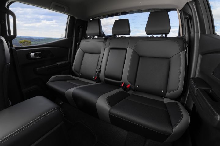 Rear cabin view of a 2026 Nissan Navara ST‑X showing the three-seat rear bench, adjustable headrests, seatbelts, door trims, and the rear window with a rural landscape visible outside.
