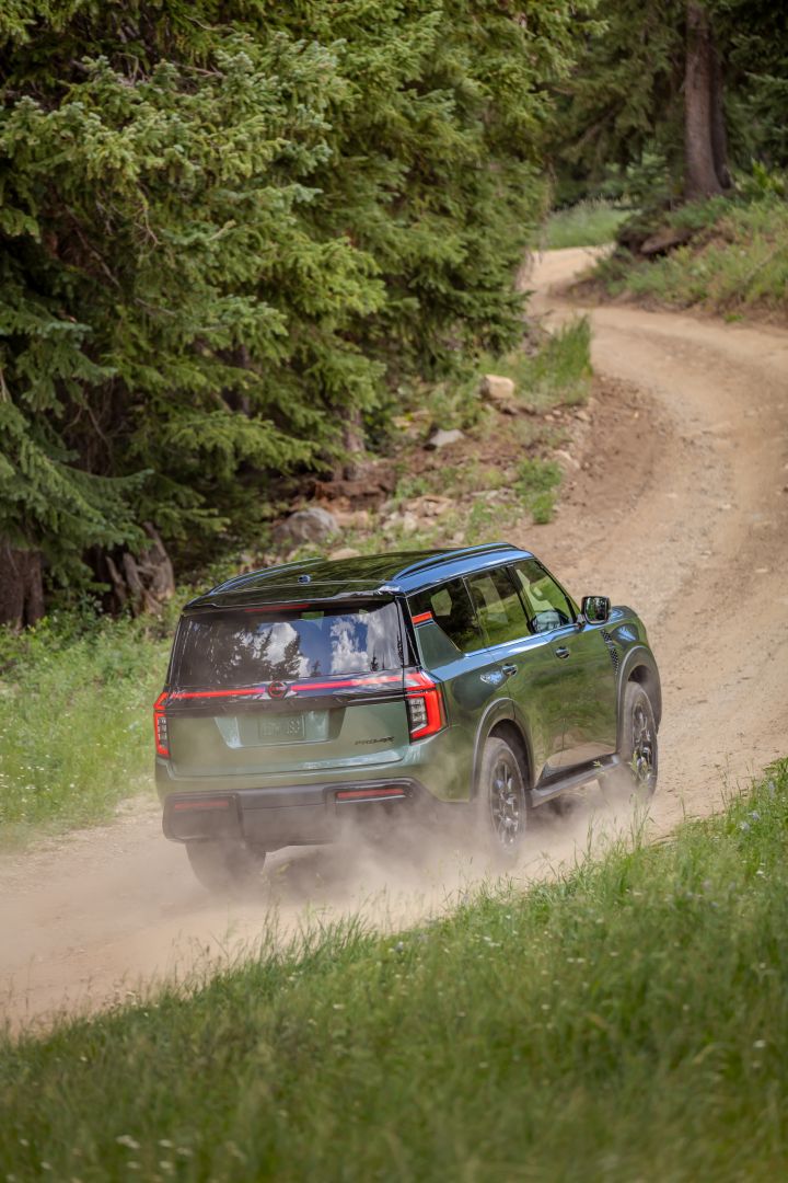 Right rear 3/4 angle of the 2025 Nissan Armada driving down a dirt path. dust flies up from speed.