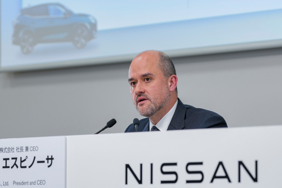 Nissan-CEO Ivan Espinosa spricht auf einer Pressekonferenz. Auf dem weißen Hintergrund ist ein Bild eines Autos zu sehen, davor ein Schild mit der Aufschrift „NISSAN“ und Mikrofone. Er trägt einen Anzug und blickt nach vorne.