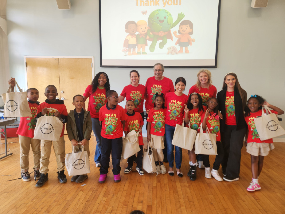 A group of children stand smiling, gathered for a photo with Nissan employees.