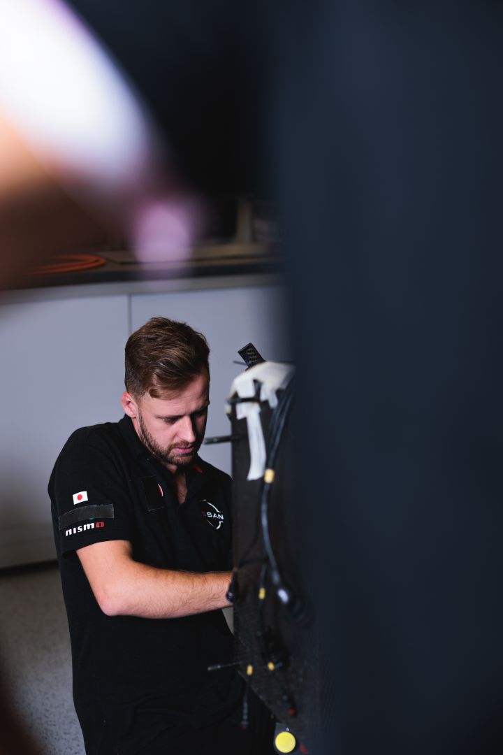Unscharfer schwarzer Vordergrund, im Hintergrund Fokus auf einen arbeitenden Nissan Formel E Mechaniker
