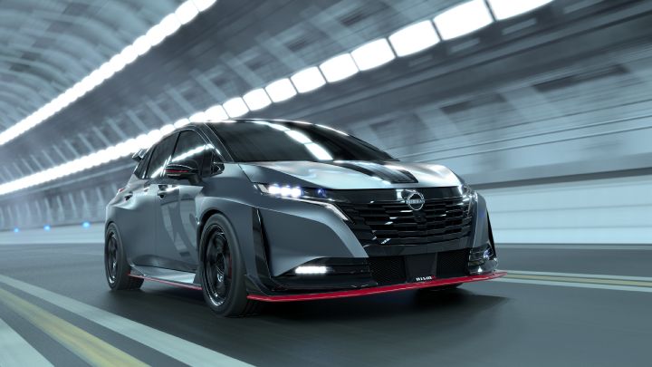A silver and black two-tone sports car, the Aura Nismo RS Concept, speeding through a tunnel in a front-left angled view. The vehicle features a low stance and sharp front design, with the Nissan logo on the center grille and a red accent line with the 'NISMO' logo on the lower bumper. The hood has black stripes, and the black wheels with red brake calipers stand out. The tunnel walls appear blurred in the background, emphasizing motion and speed