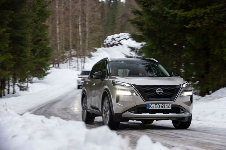 Silberner Nissan X‑Trail e‑Power e‑4ORCE kommt aus einer schneebedeckten Kurve herausgefahren